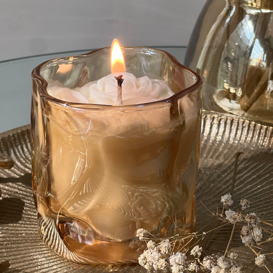 Jasmine Scented Candle in a golden glass holder with dried flowers on a reflective surface