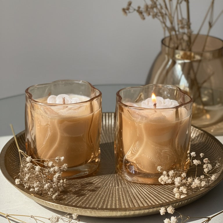 Two lit candles in glass holders on a decorative tray with dried flowers.