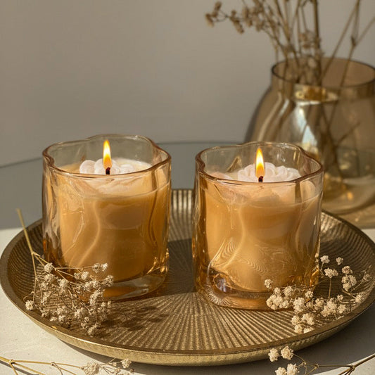 Two lit candles in glass holders on a decorative tray with dried flowers.