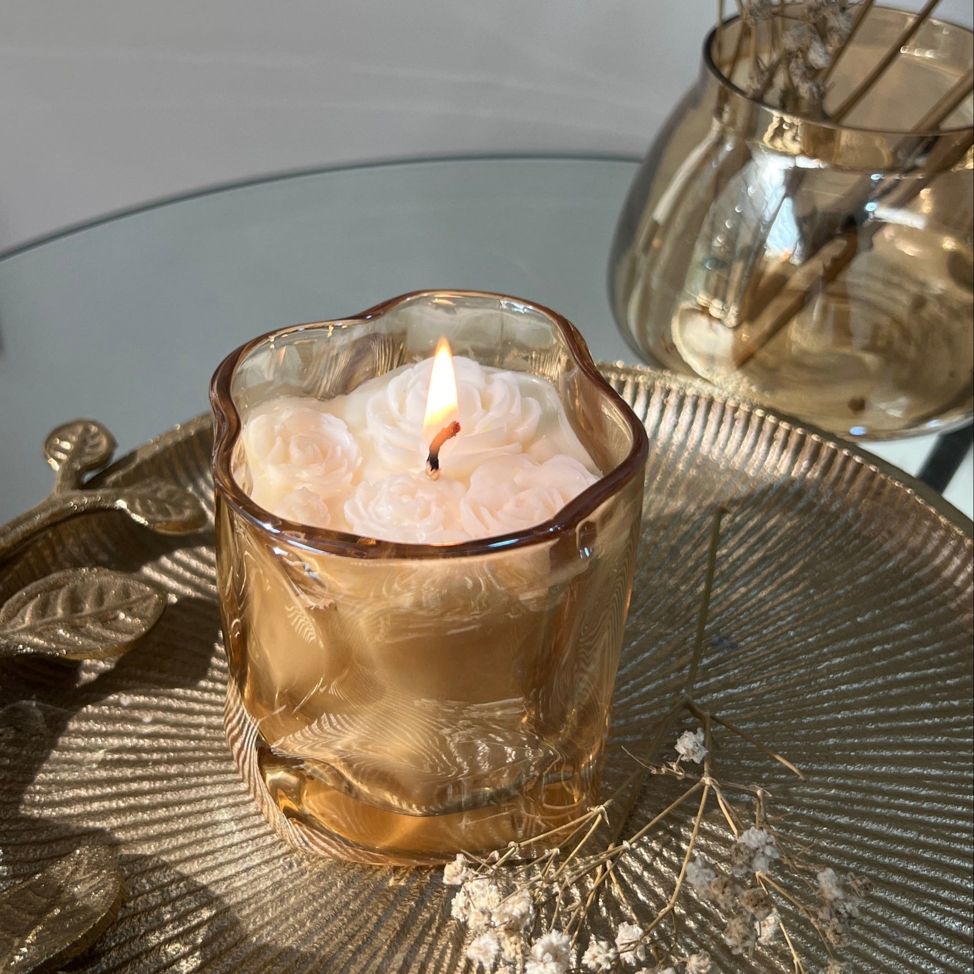 Candle in a textured glass holder on a decorative tray with dried flowers.