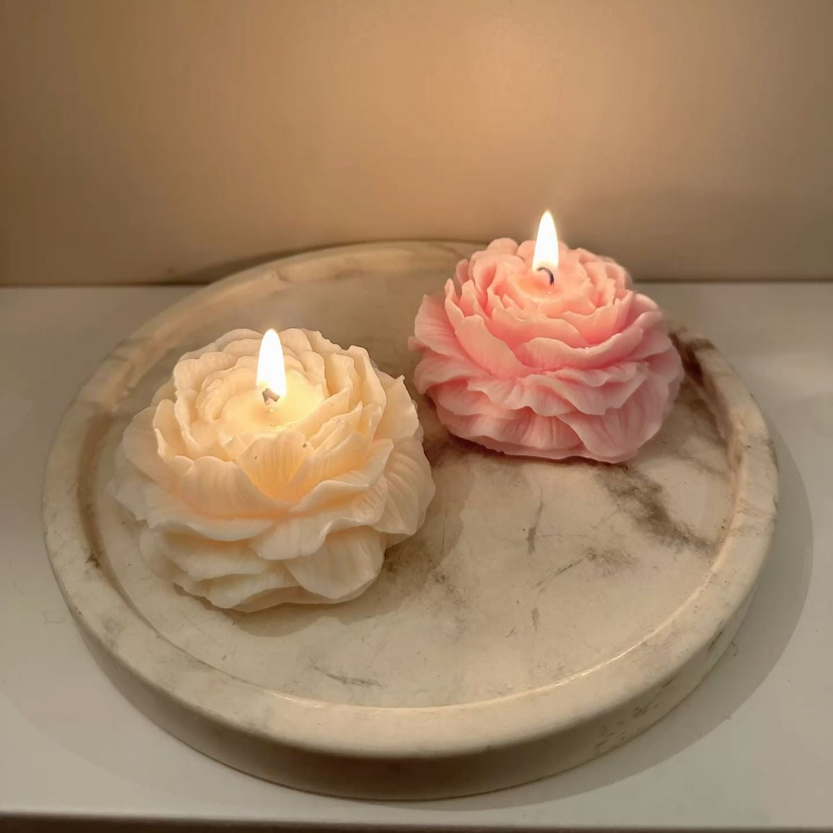 Two flower-shaped candles on a marble surface with a soft background