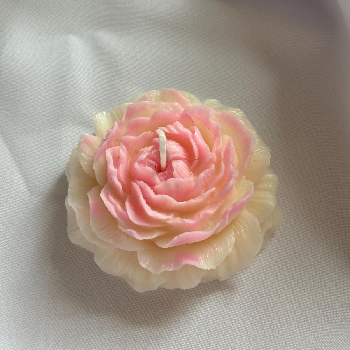 Pink Peony-shaped candle on a white fabric background