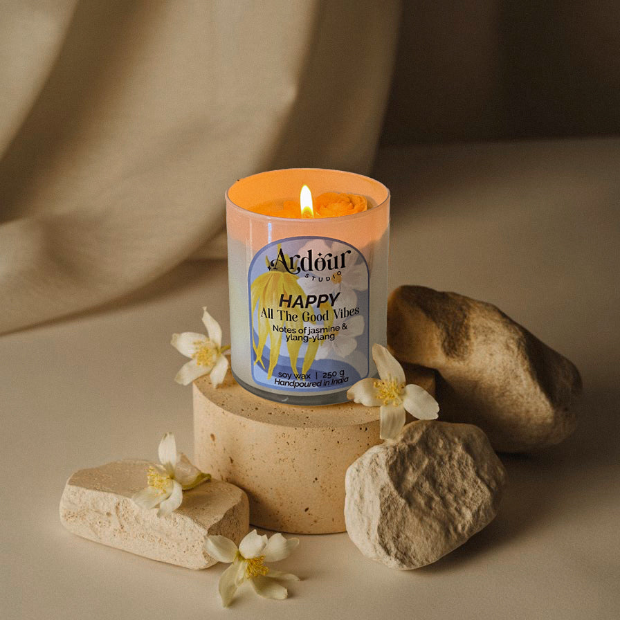 A lit candle in a decorative container with flowers and rocks on a neutral background