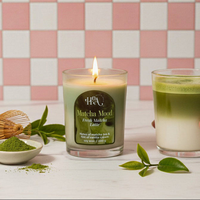 Matcha-themed candle and glass of matcha latte on a checkered pink and white wall background