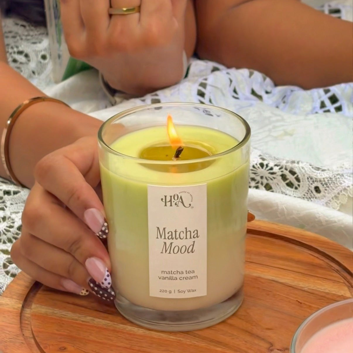 Person holding a lit candle labeled 'Matcha Mood' with another candle in the background.