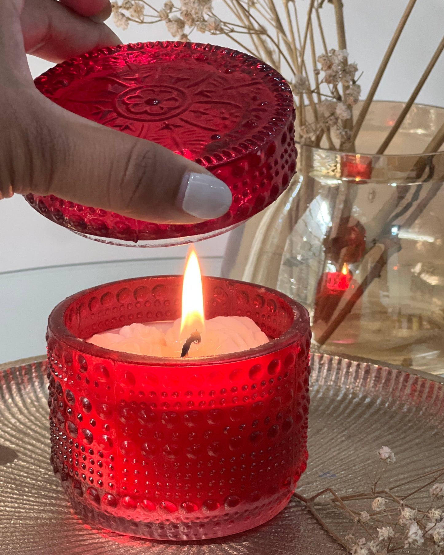 Red textured candle holder with a lit candle, held by a hand, on a reflective surface.