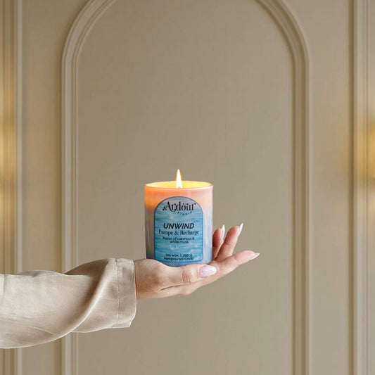 Hand holding a lit candle labeled 'Unwind' against a neutral wall.