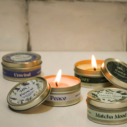 Small candles in tin containers with labels on a light surface.
