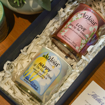 Two candles in a decorative box with flowers in the background