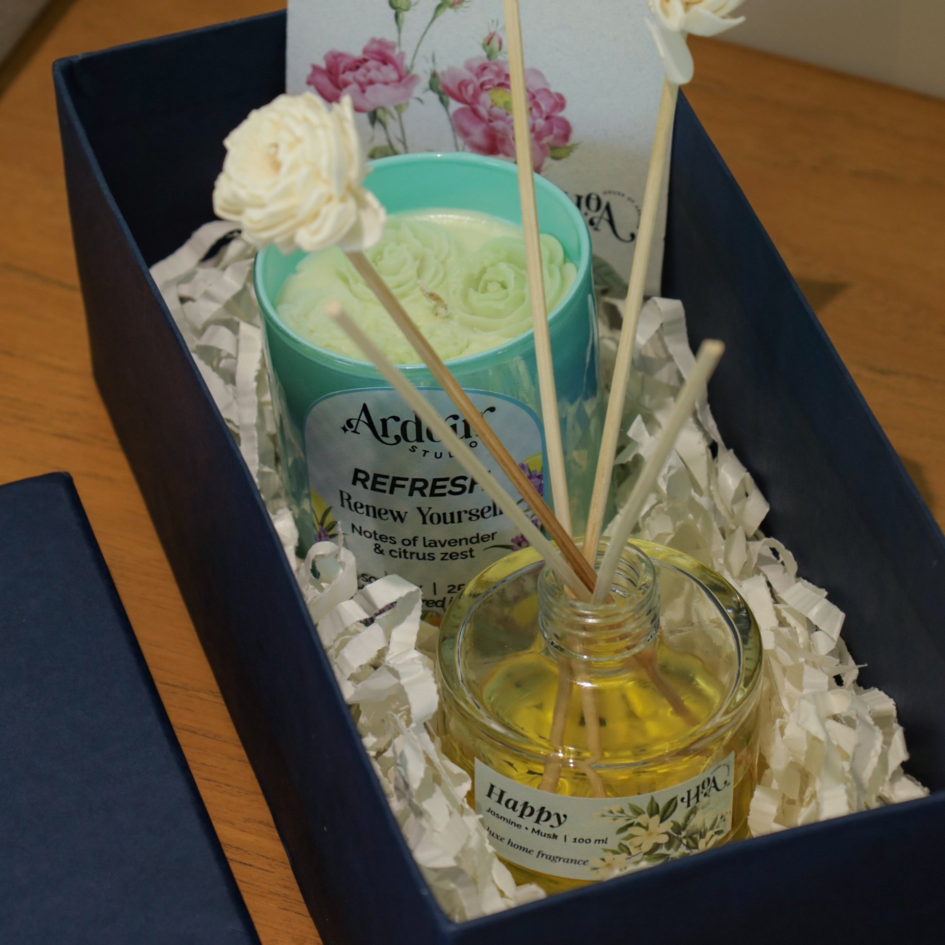 Gift set with diffuser, candle, and card in a box on a wooden surface.