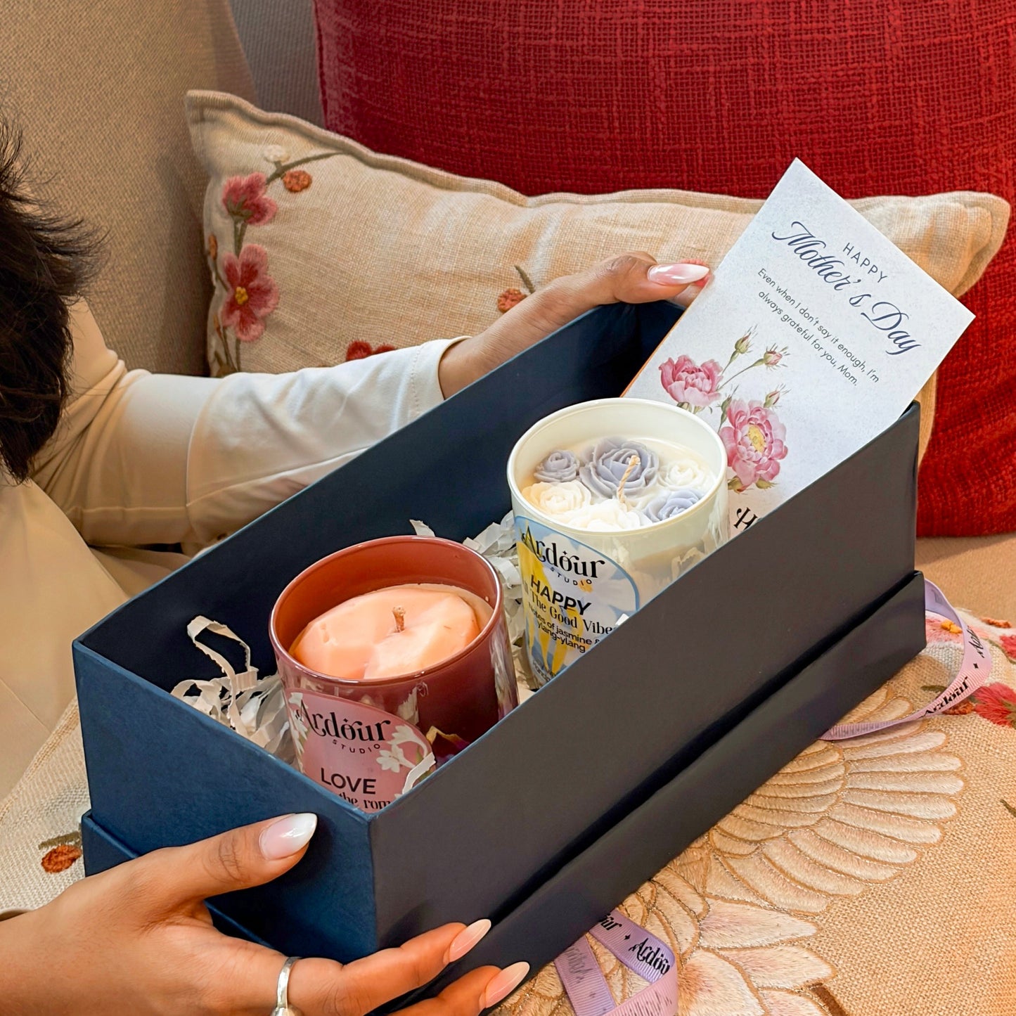 Gift box with candles and a card on a floral-patterned surface