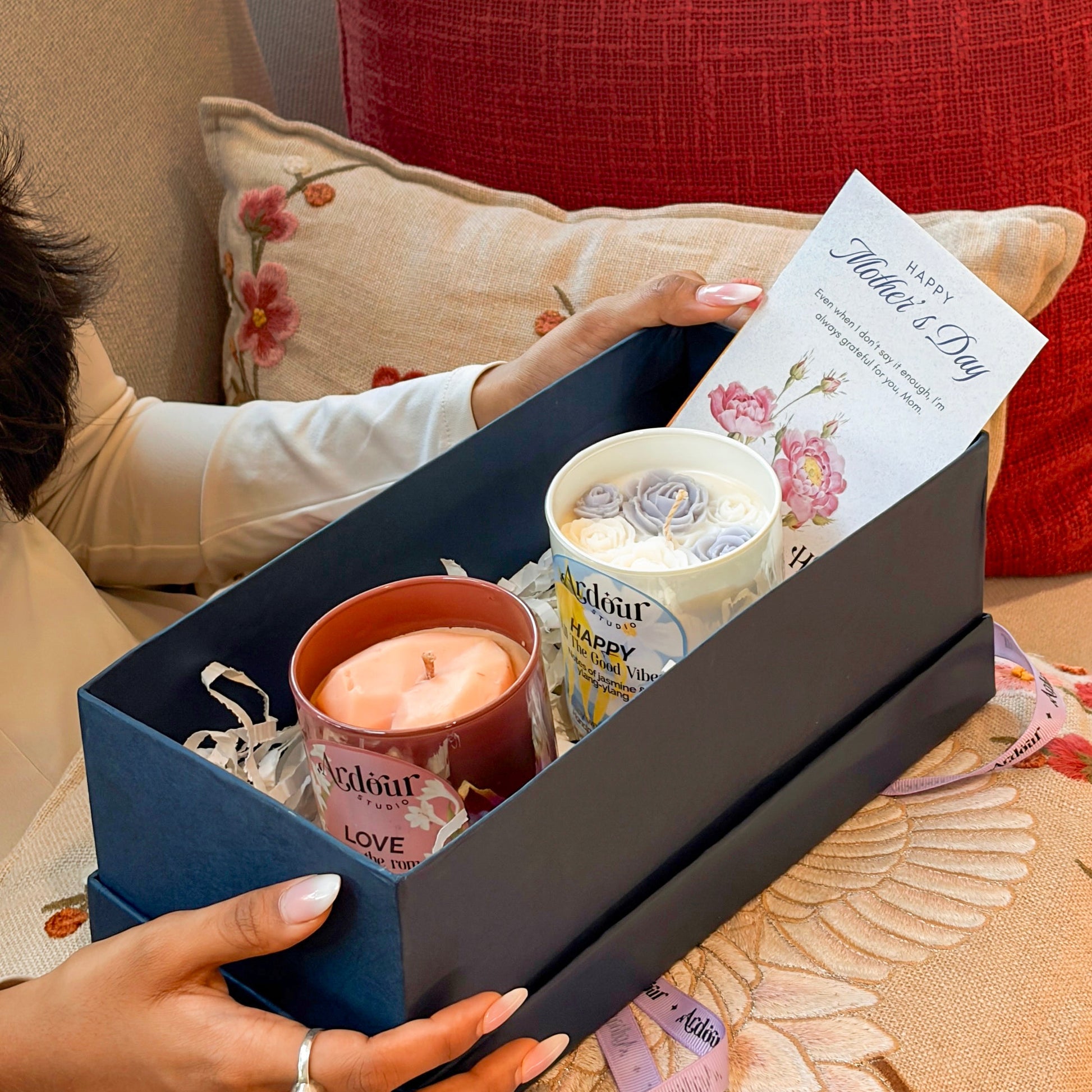 Gift box with candles and a card on a floral-patterned surface