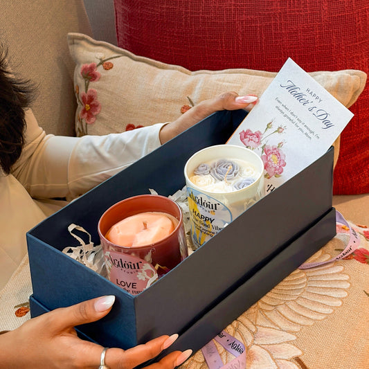 Gift box with candles and a card on a floral-patterned surface
