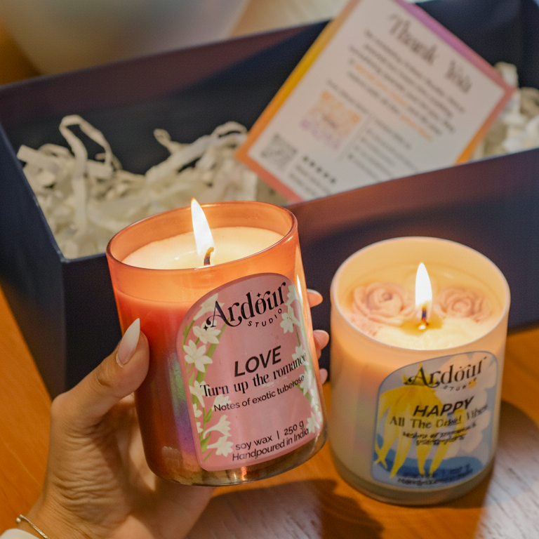 Two Aroma Lite candles being held with a box and flower arrangement in the background