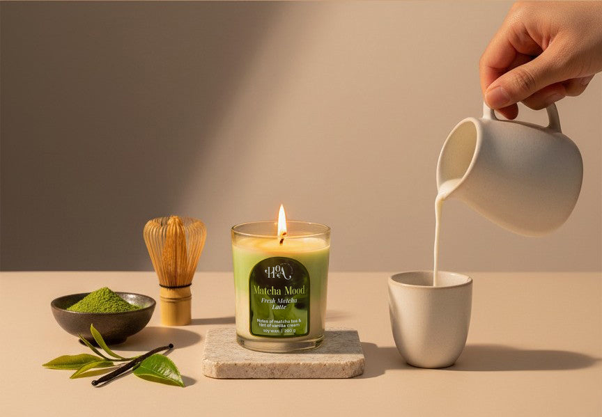 Scented Candle labeled 'Matcha Mood' with a hand pouring milk into a cup, surrounded by matcha leaves and a whisk.
