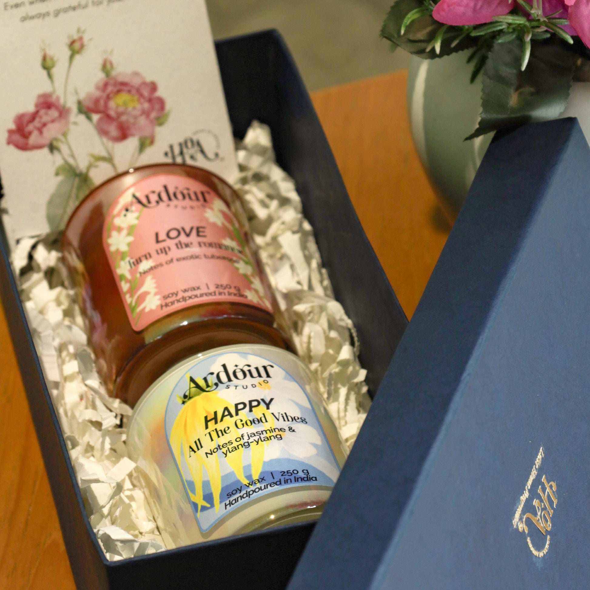 Gift set with aromatherapy candles and Mother's Day card next to a vase of flowers.