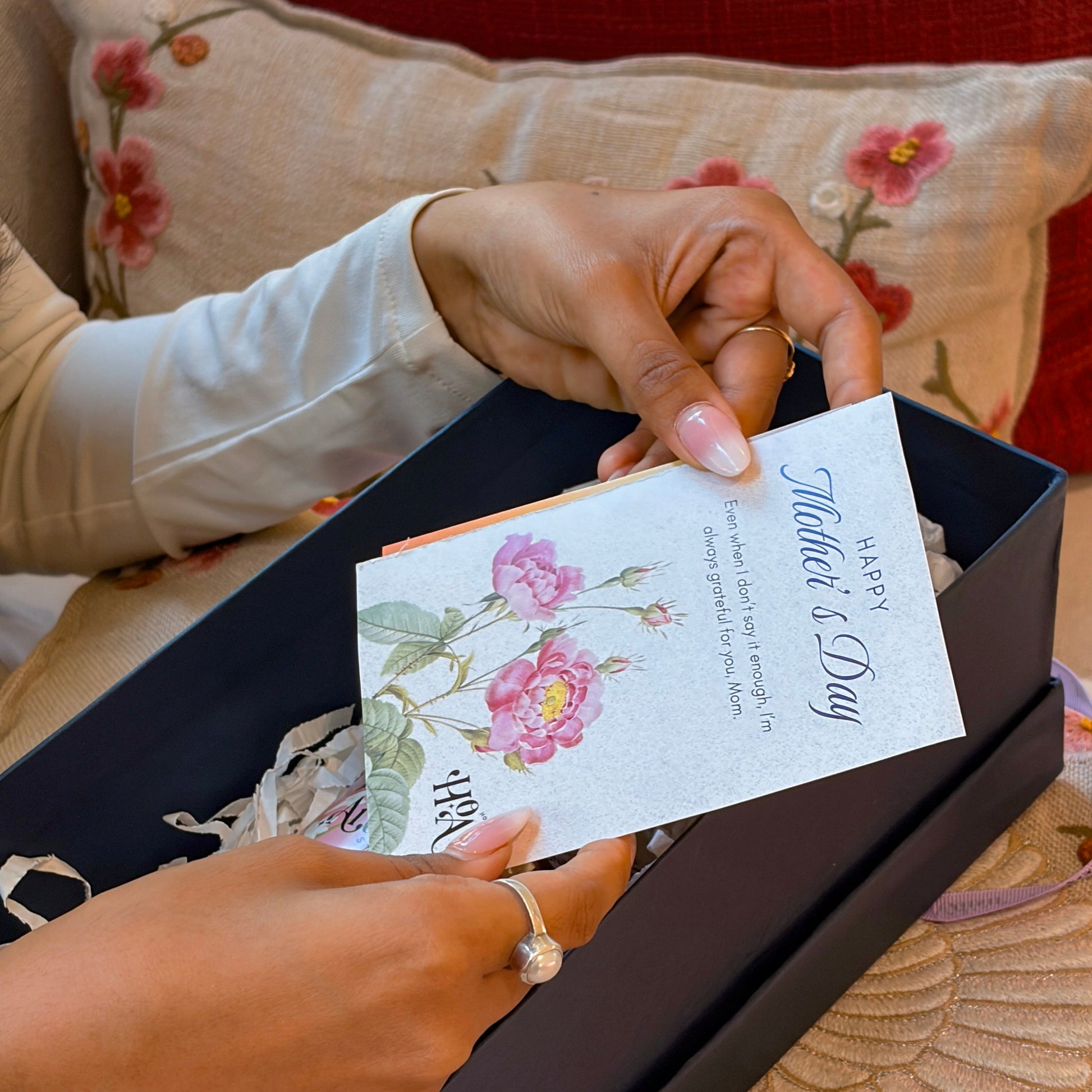 Person holding a card with floral design and 'Thank you' message, sitting on a floral-patterned surface.