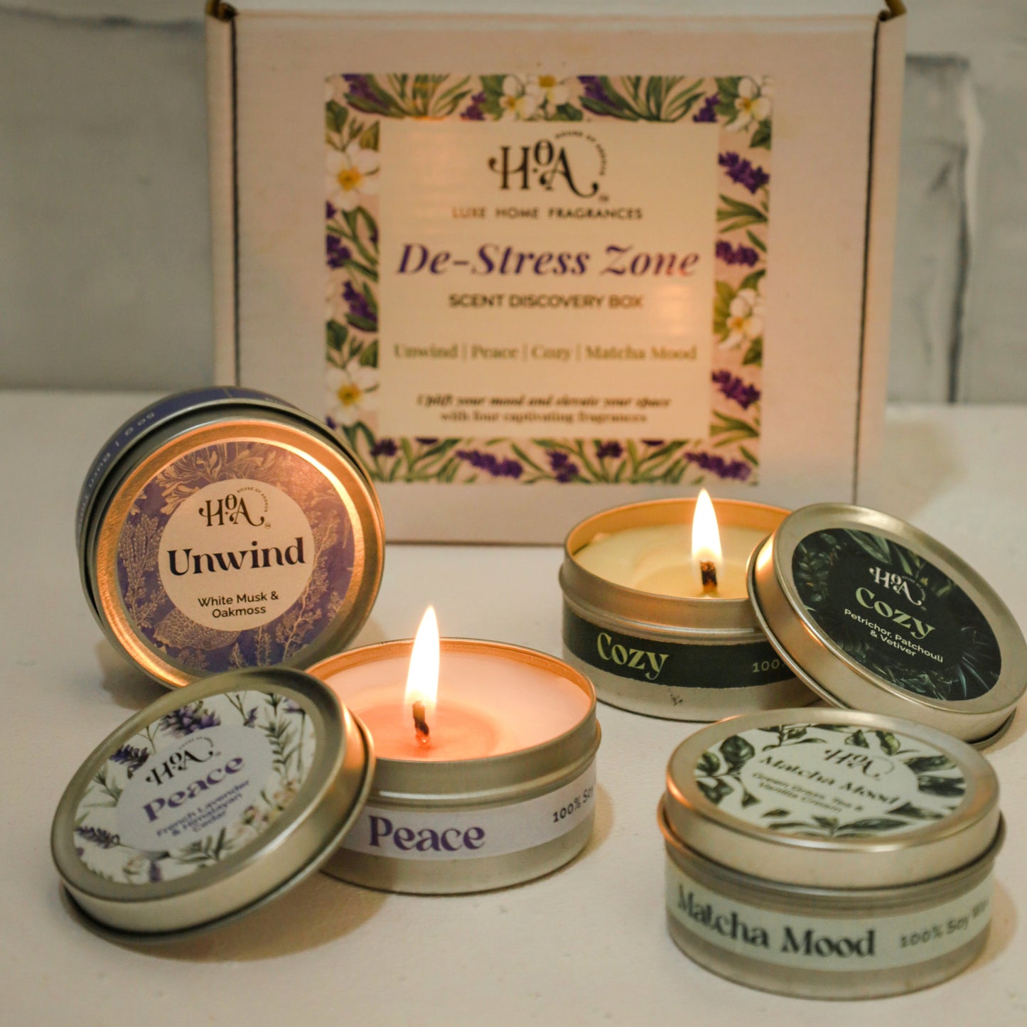 Set of small candles with lids featuring text, one lit, against a neutral background.