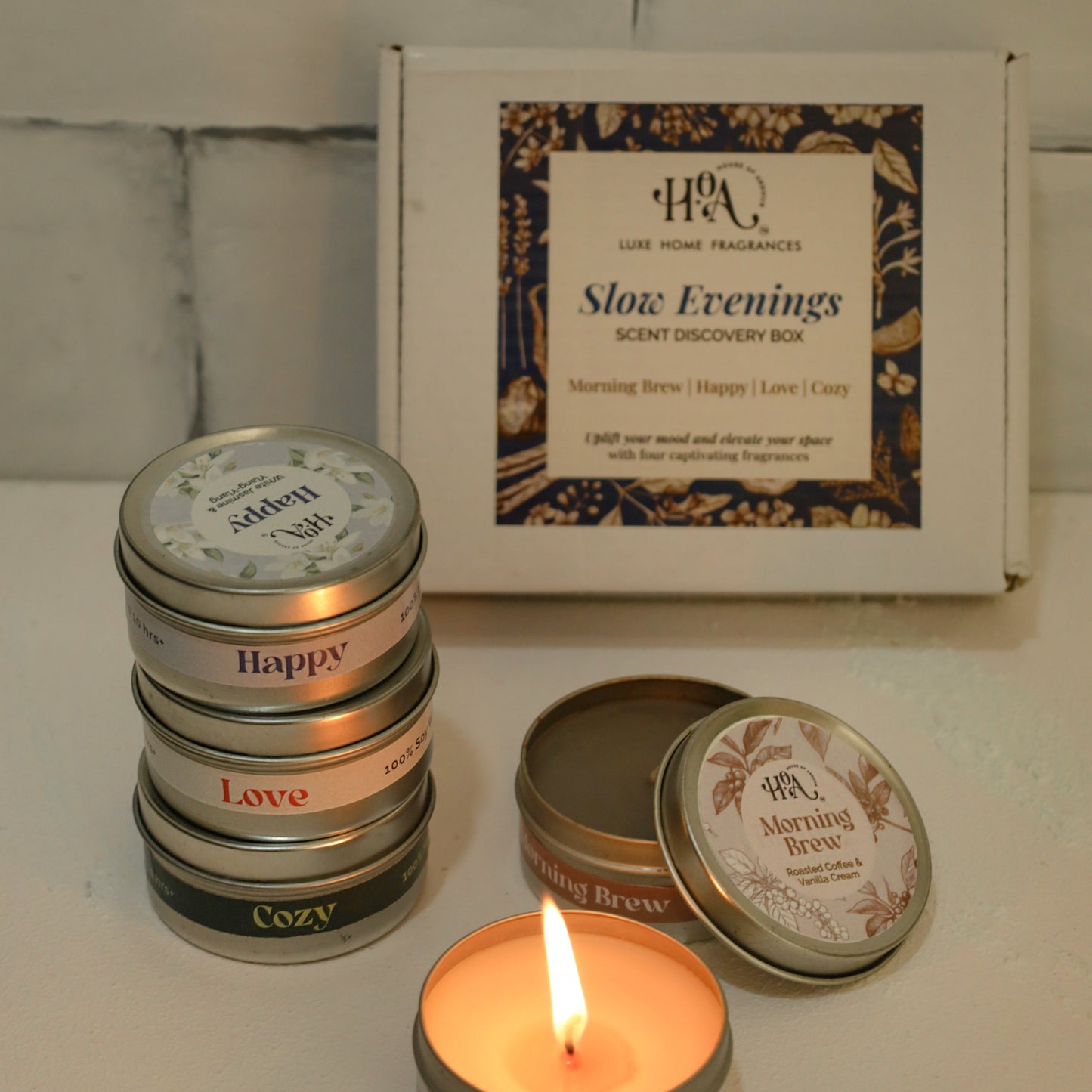 Set of small candles in tins with a box labeled 'Slow Evenings' on a tiled wall background.
