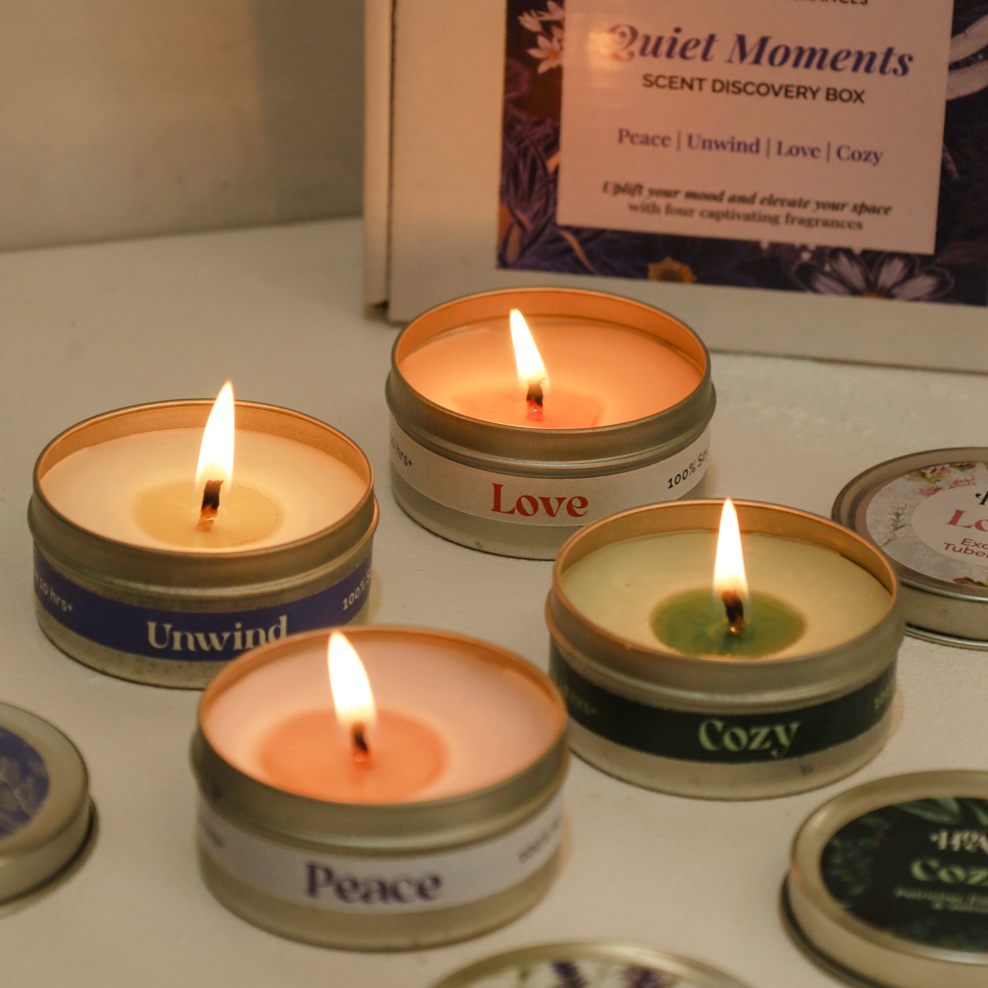 Set of small candles in tin containers with visible labels on a white surface.