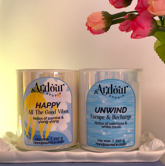 Two scented candles- Happy and Unwind floral decorations on a table.
