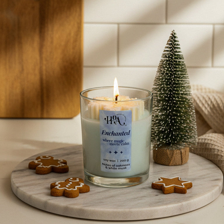Candle with a label on a marble surface with a small Christmas tree and gingerbread cookies.