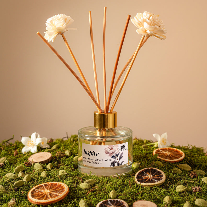 Diffuser with floral sticks on a decorative surface with flowers and oranges and cardamom.