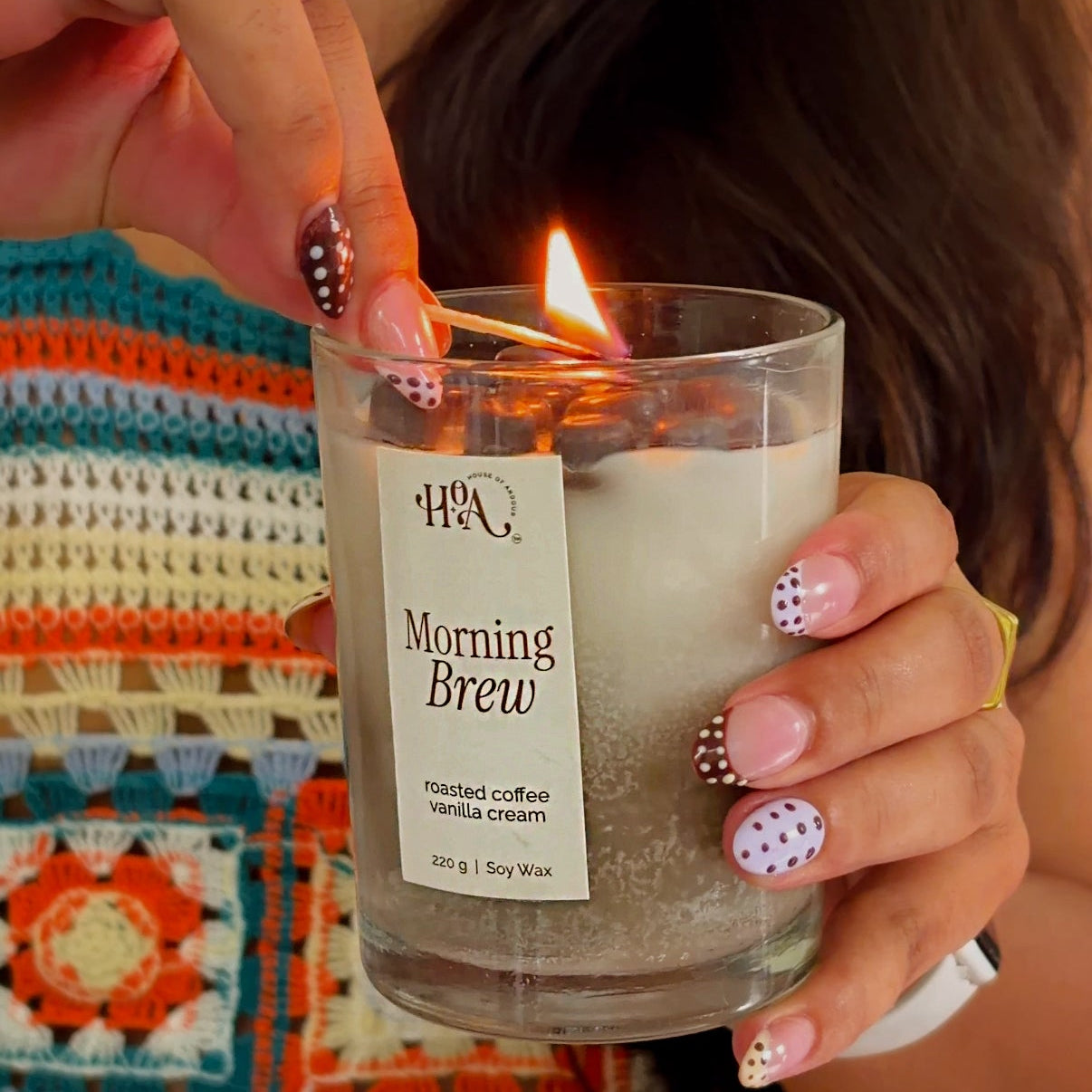 Person lighting a candle labeled 'Morning Brew' with colorful background