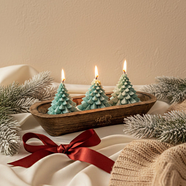 Three small green Christmas tree-shaped candles in a wooden tray with a red ribbon on a white surface.