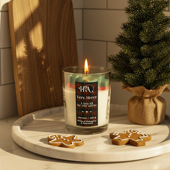 Candle with a Christmas label on a marble surface with a small tree and cookies.